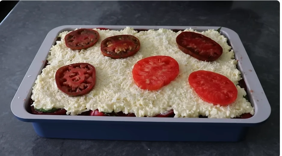 Cheese topping spread over tomato Frito pie with tomato slices on top
