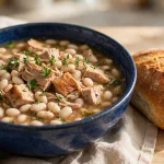 Turkey and bean soup with navy beans in a blue bowl with crusty bread
